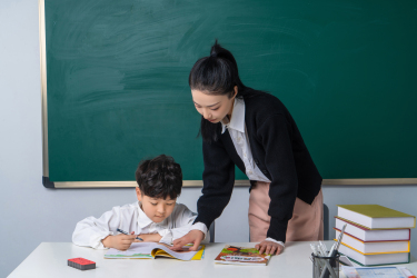 认真做功课的学生和站立的女老师高清图