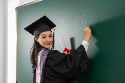 穿博士服往黑板写字的毕业生高清图