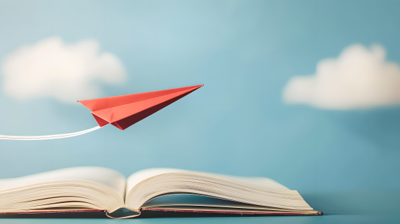 红色纸飞机从书本上飞过，天蓝色的摄影图片